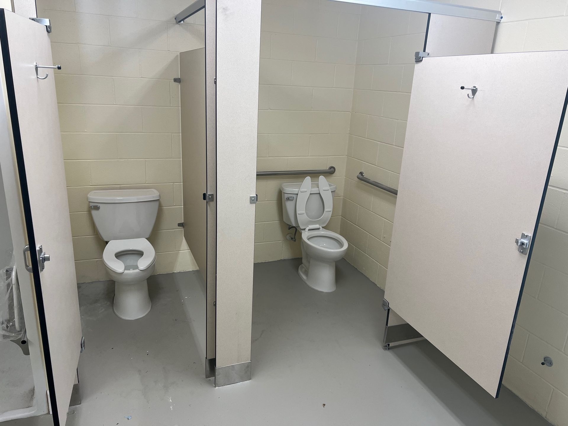Public restroom with white stalls, two toilets, and gray floors and walls.