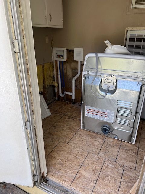 Laundry room with exposed wall, plywood floor, and a dryer.