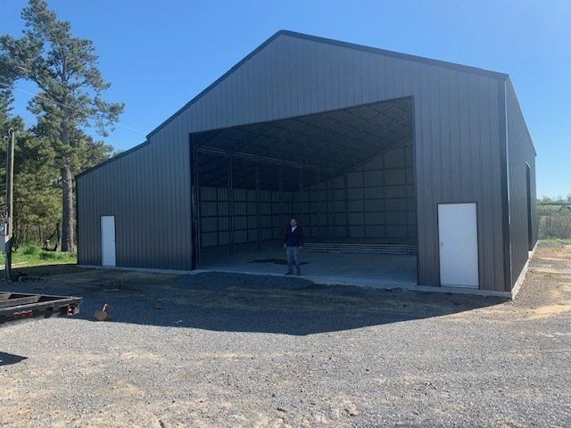 Large gray metal barn with open front and white doors; person stands inside.