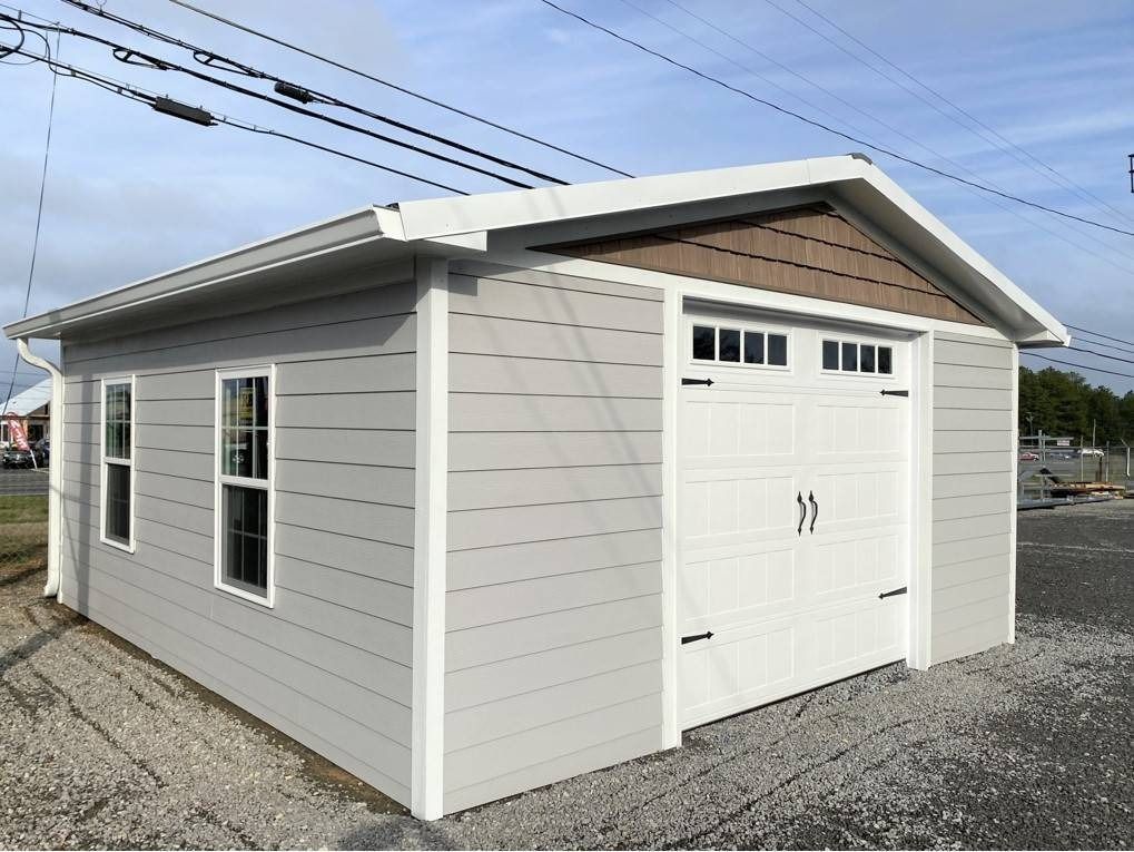 Gray shed with white trim, brown gable. Two windows on left, garage door on front.
