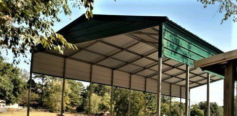 Green metal carport structure with trees in the background under a blue sky.