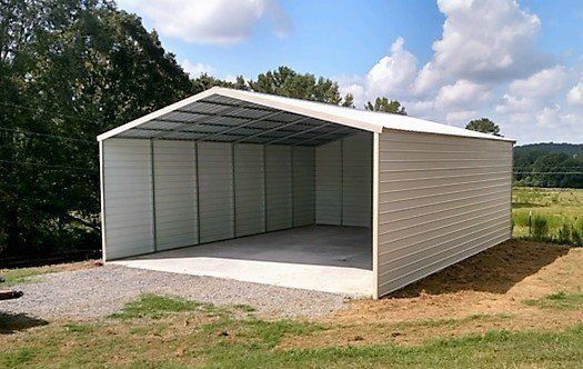 Metal carport on gravel driveway with open front, grassy yard, and trees.