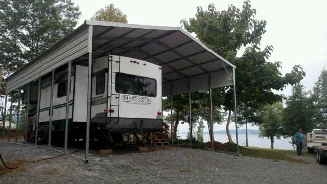 RV parked under a metal carport next to a body of water.