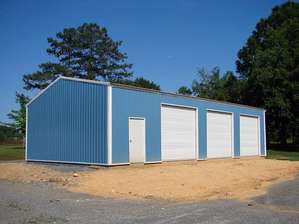 Blue metal garage building with four garage doors and a side door, on a gravel surface.
