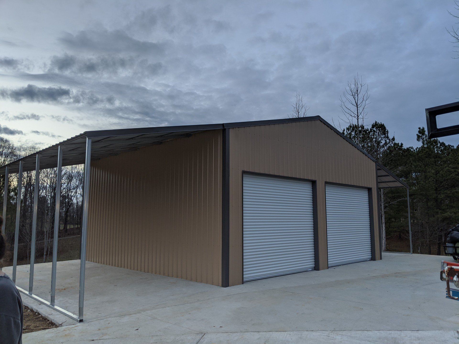 Tan metal building with two garage doors and a carport, concrete slab, outdoors.