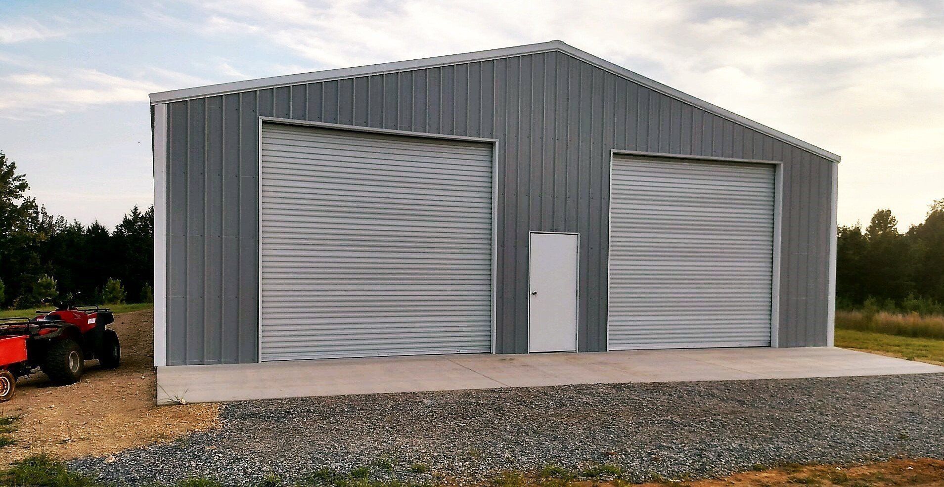 Gray metal building with two garage doors and a white door, set on gravel.