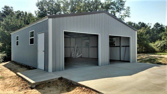 Gray metal two-car garage with open bays, concrete driveway, and small windows.