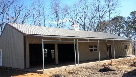 Tan metal building with carport, two garage doors, and small cupola.