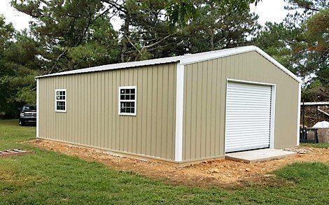 Tan metal storage shed with white trim, roll-up door, two small windows, on a concrete base, grassy yard.