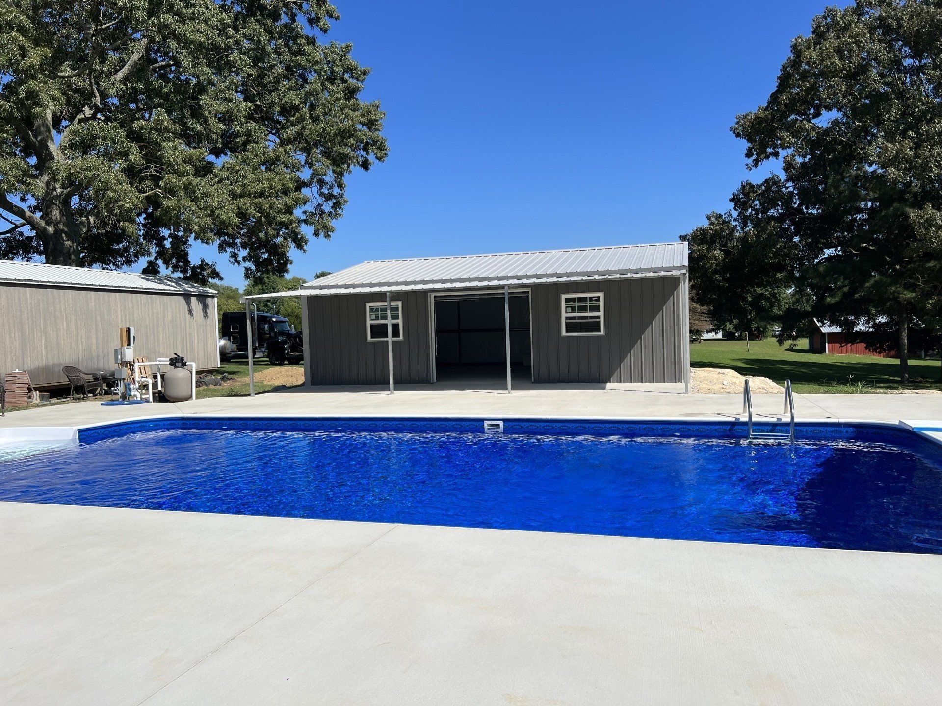 Swimming pool with a blue surface, a gray shed and clear blue sky.