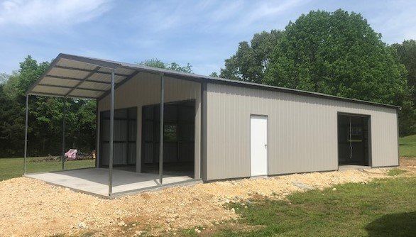 A metal carport and enclosed structure, gray siding, with a concrete pad and gravel.
