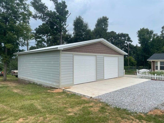 Two-car garage with white doors and light gray siding, concrete driveway, and gravel.