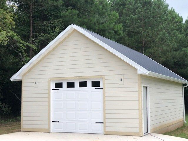 Beige garage with a white garage door, and a black shingle roof.