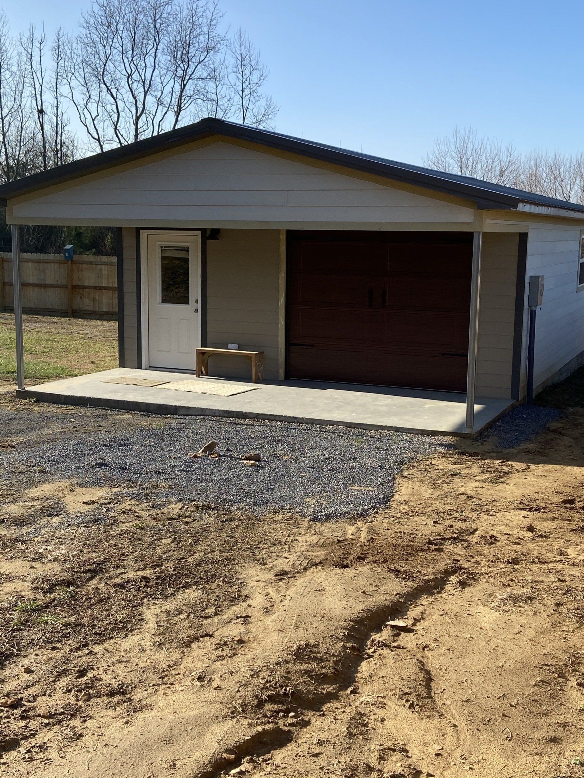 Garage with carport. Tan walls, brown roll-up door, white door, gravel driveway.
