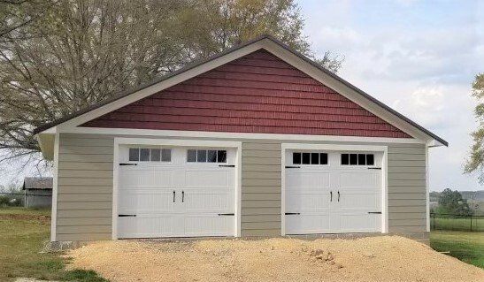 Two-car garage with white doors, tan siding, and a red shingled gable.