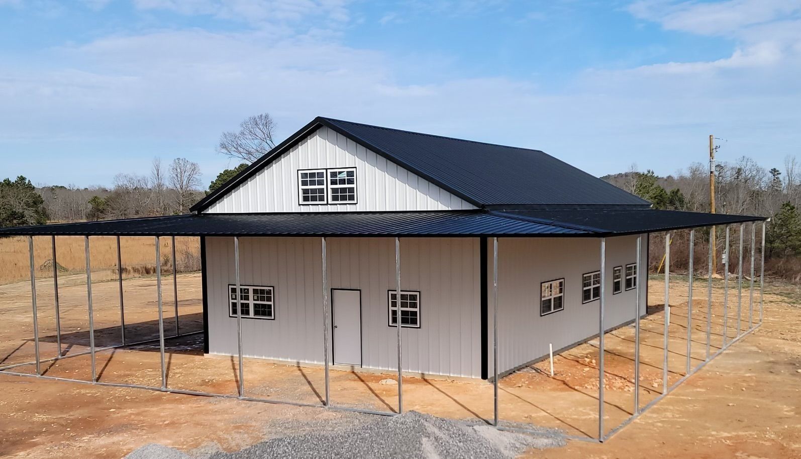 Gray metal building with black roof, white trim, and a covered porch on a sunny day.