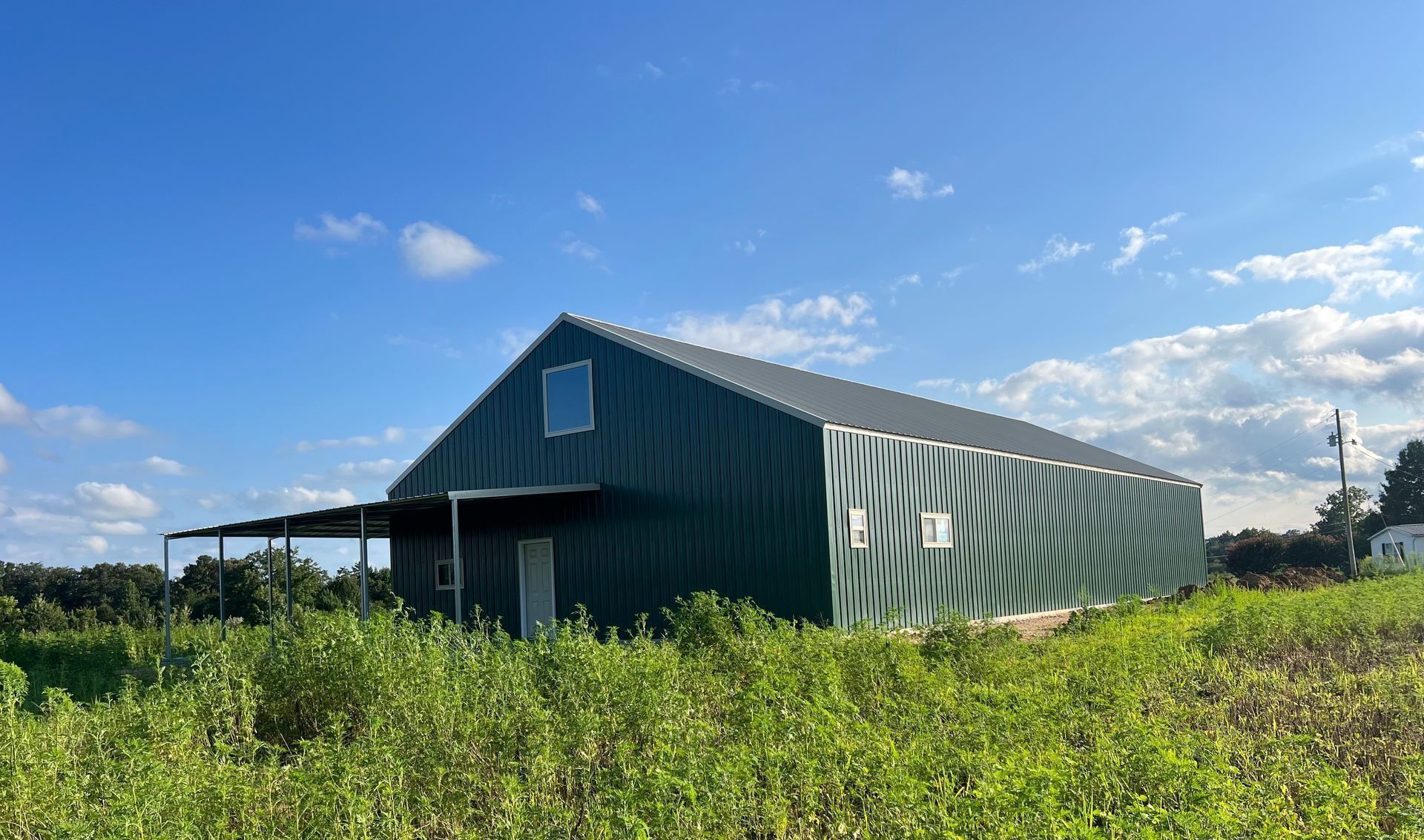 Green metal barn under a blue sky with some cloud cover. Open field in front.