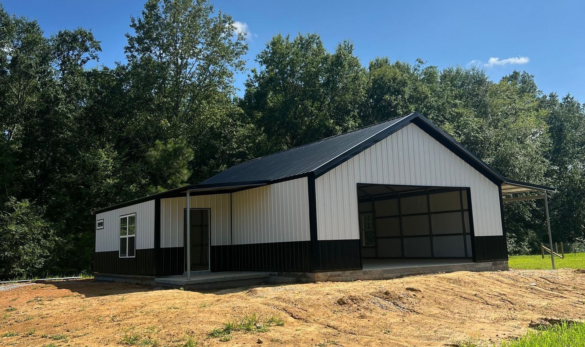 Metal building with white and black siding, open garage door, black roof, and trees in background.
