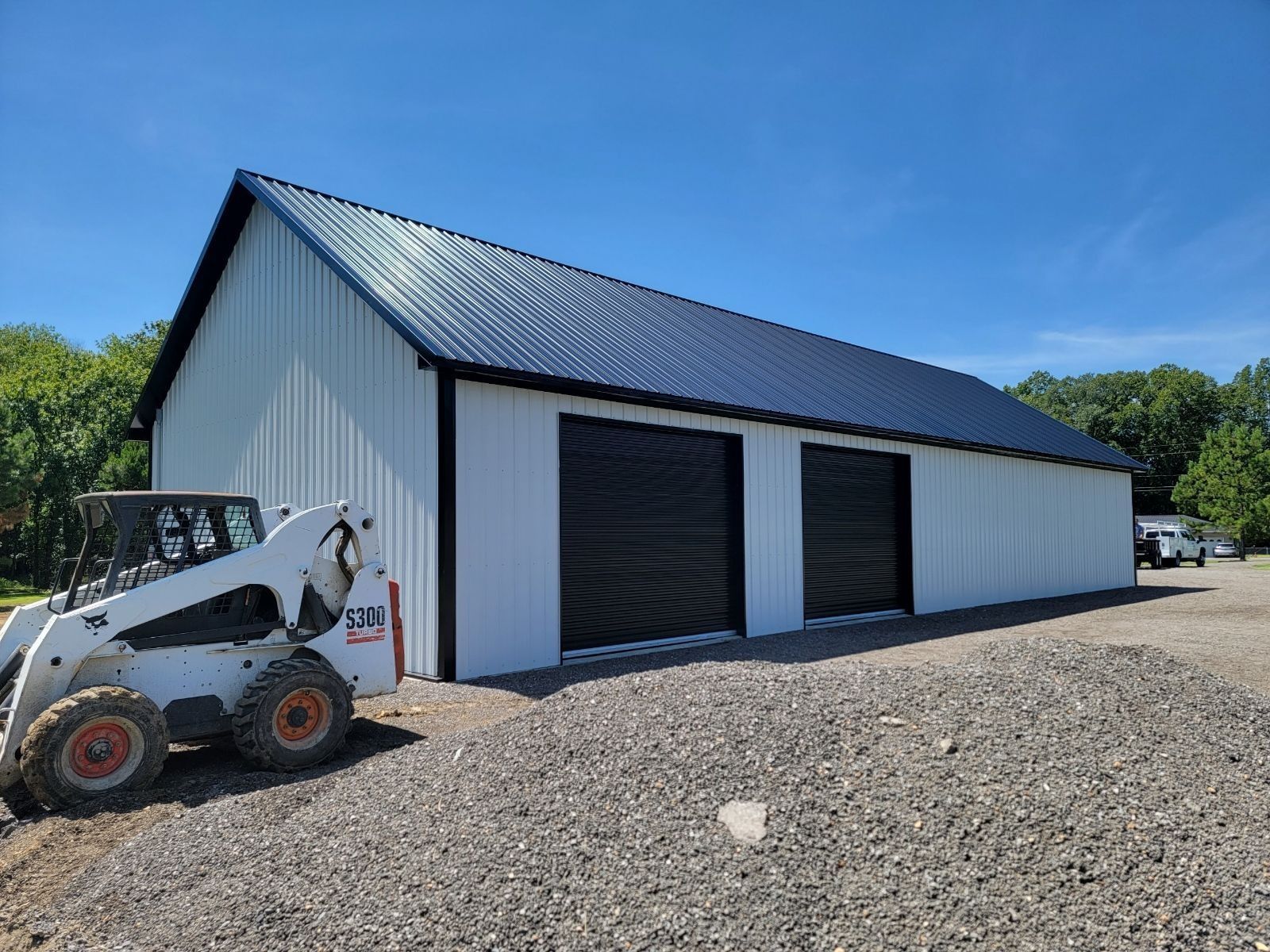 White metal building with black doors and roof, small skid steer in foreground.