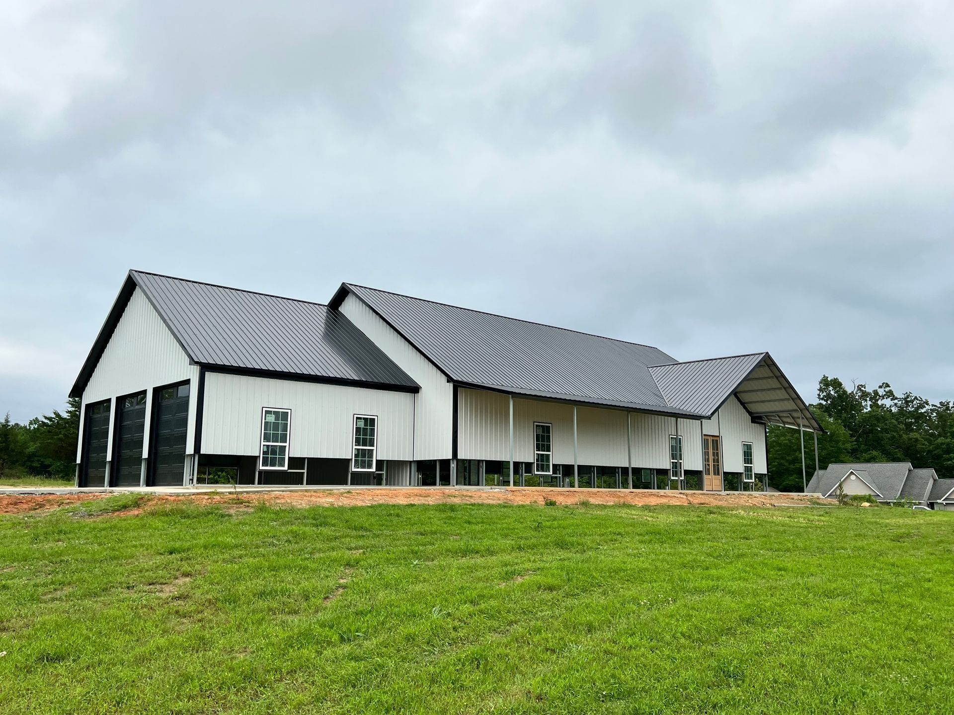 White and black barn-style building with a black roof and garage doors, set against a cloudy sky.