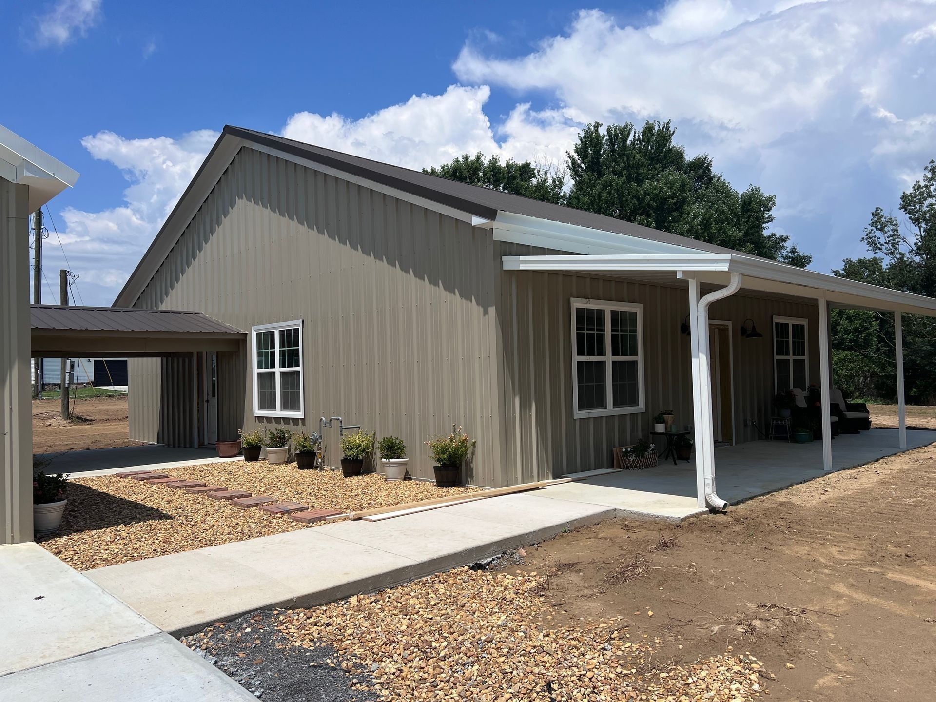 Tan metal-sided house with a carport and covered porch. Gravel landscaping, concrete walkway.