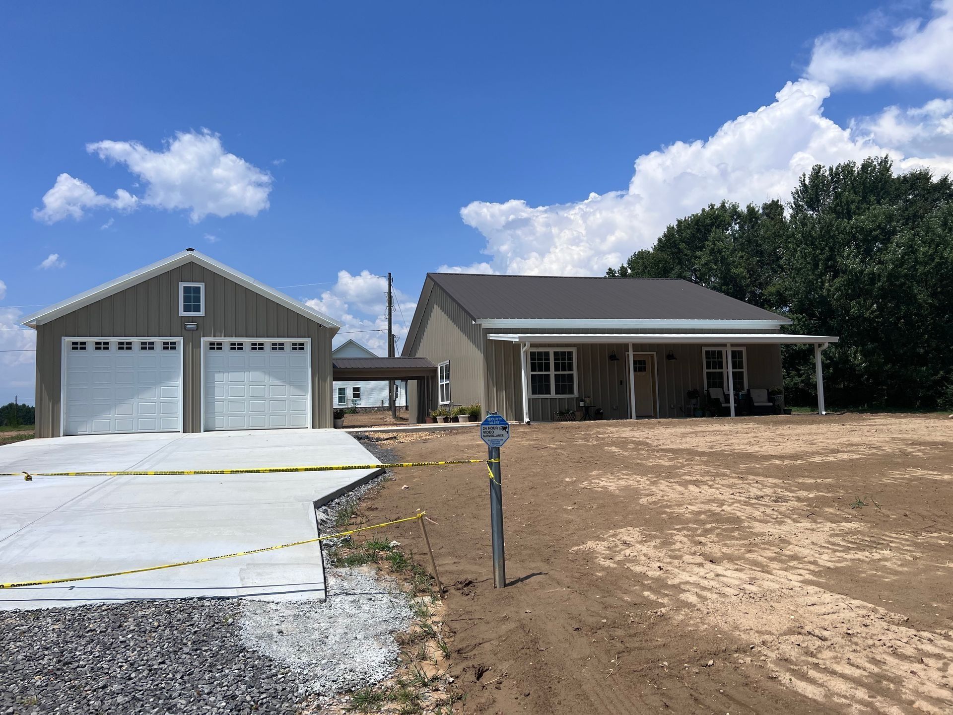 New construction house and detached garage on a dirt lot, sunny day, blue sky. Concrete driveway.