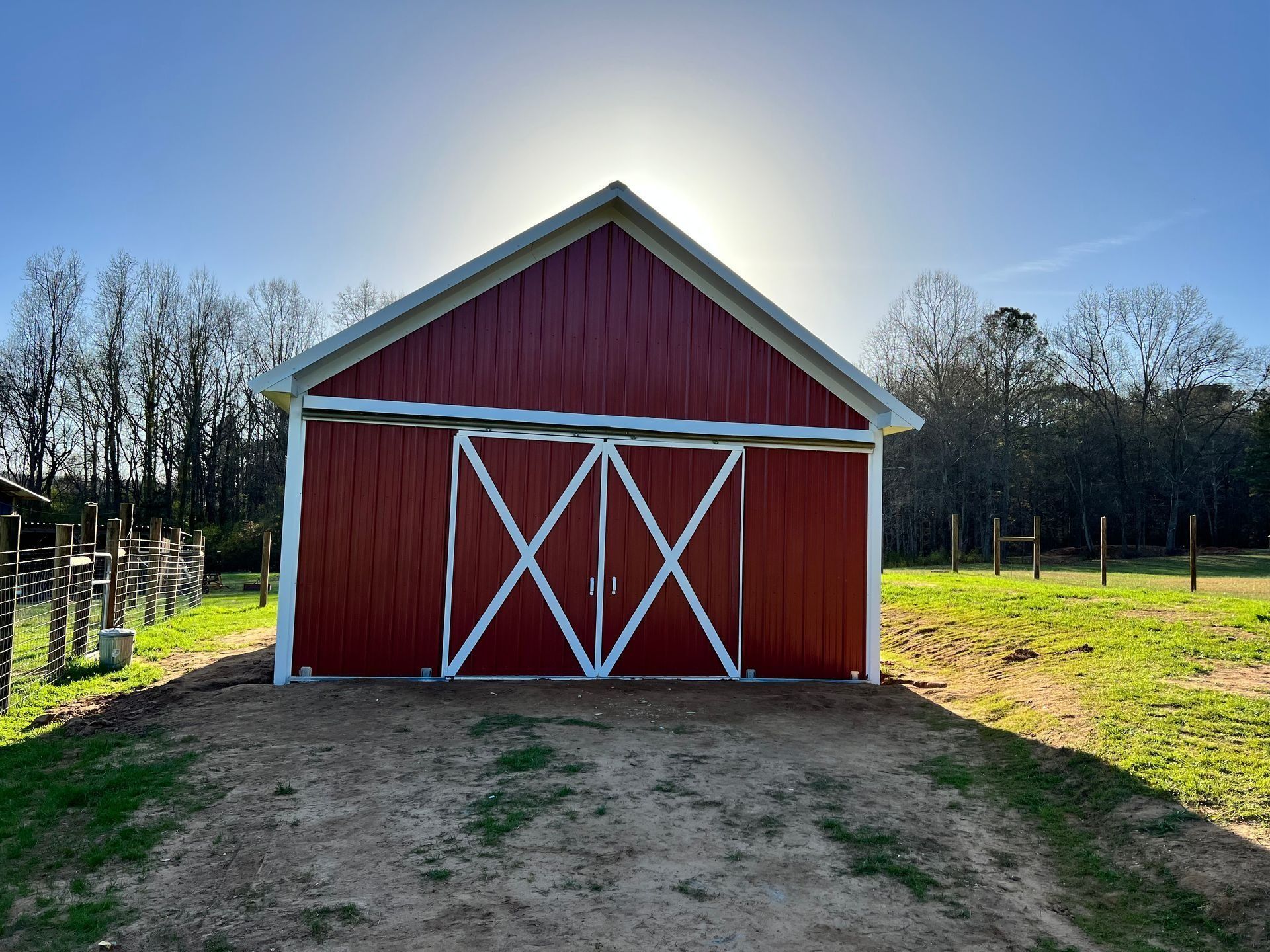 Red barn with white trim and X-pattern doors, set against a sunny sky and grassy field.