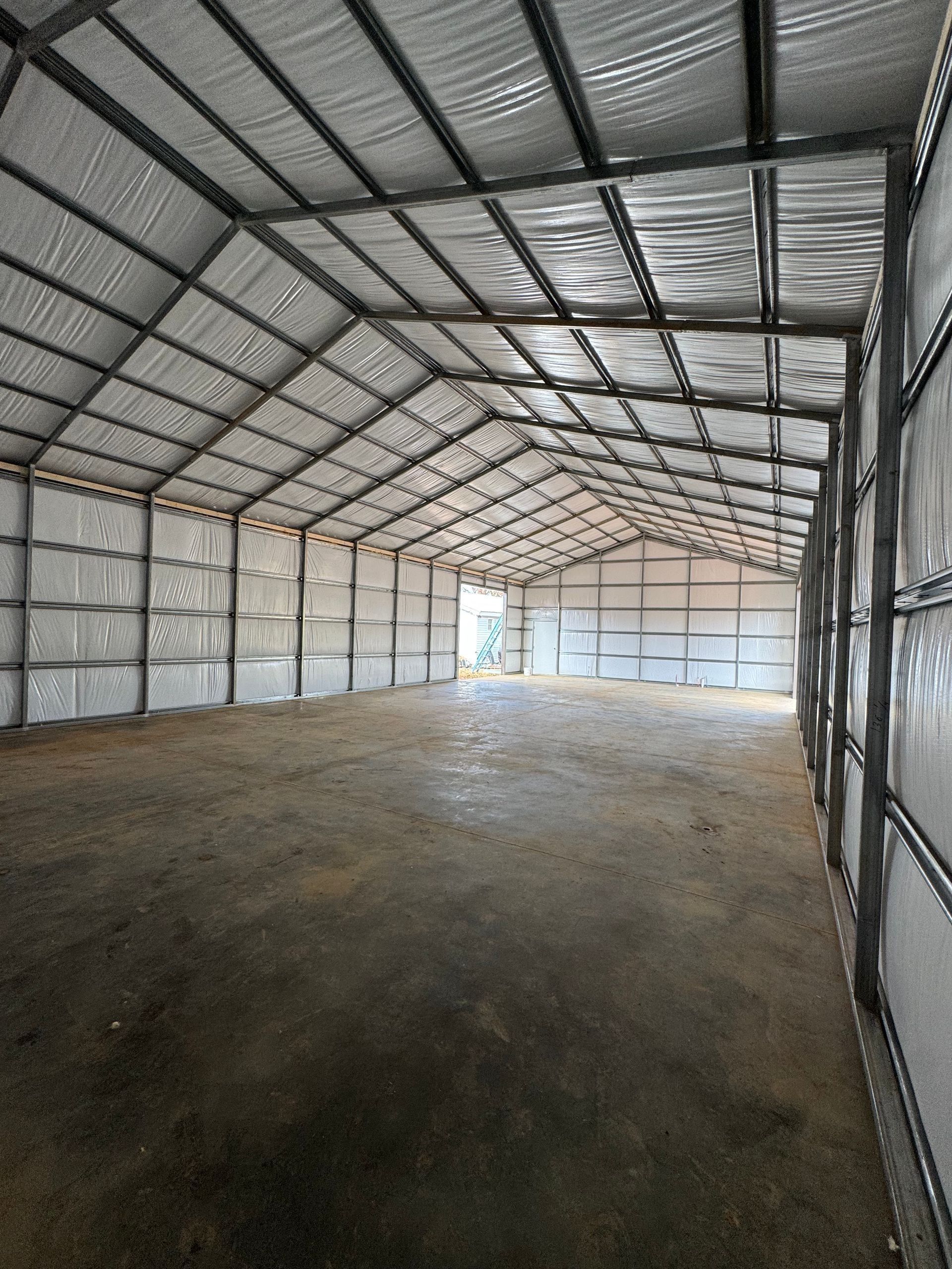 Interior view of an empty metal warehouse with a concrete floor and a high ceiling.