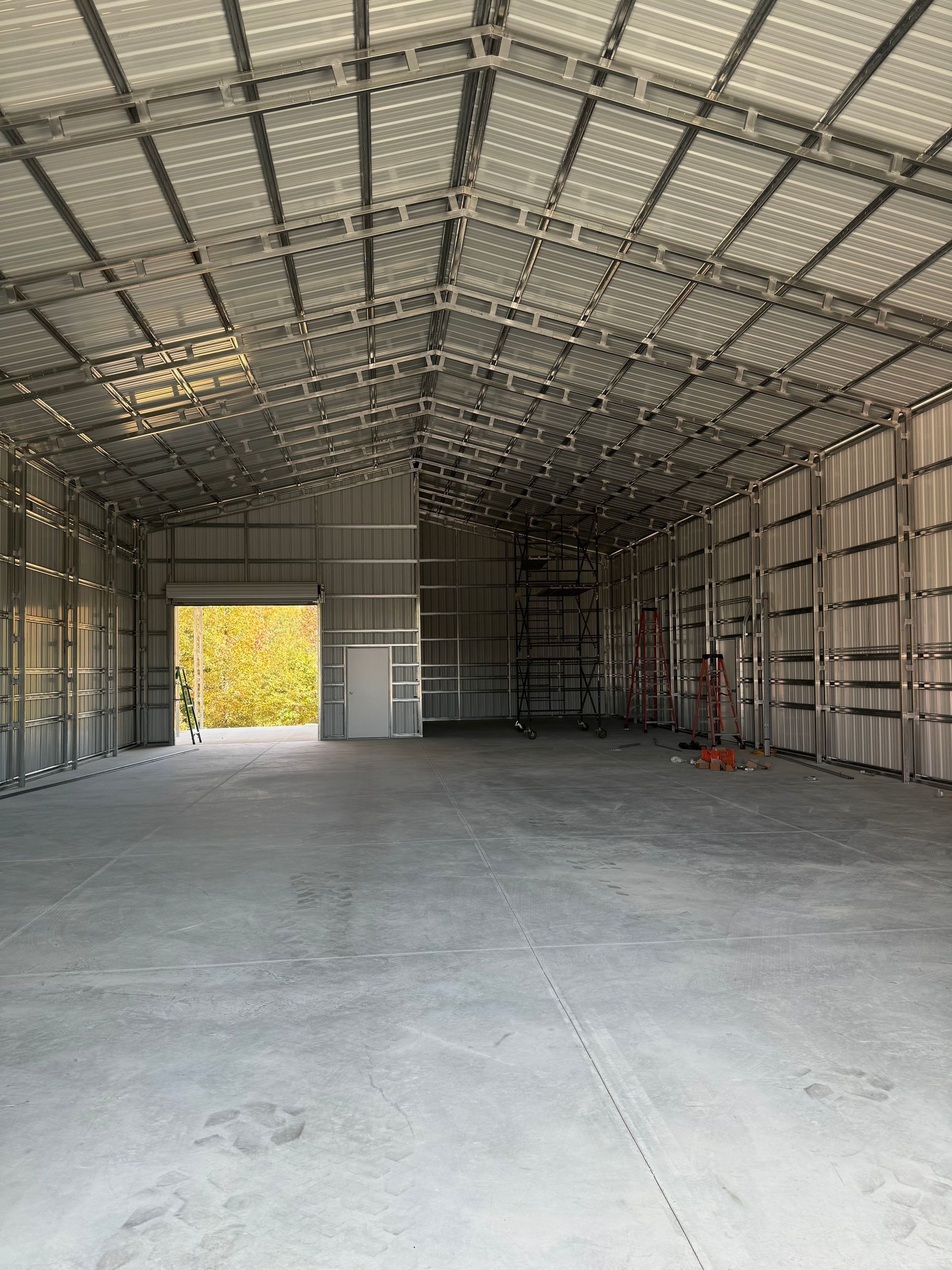 Interior of a large, empty metal building with a concrete floor and open doorway to outside.