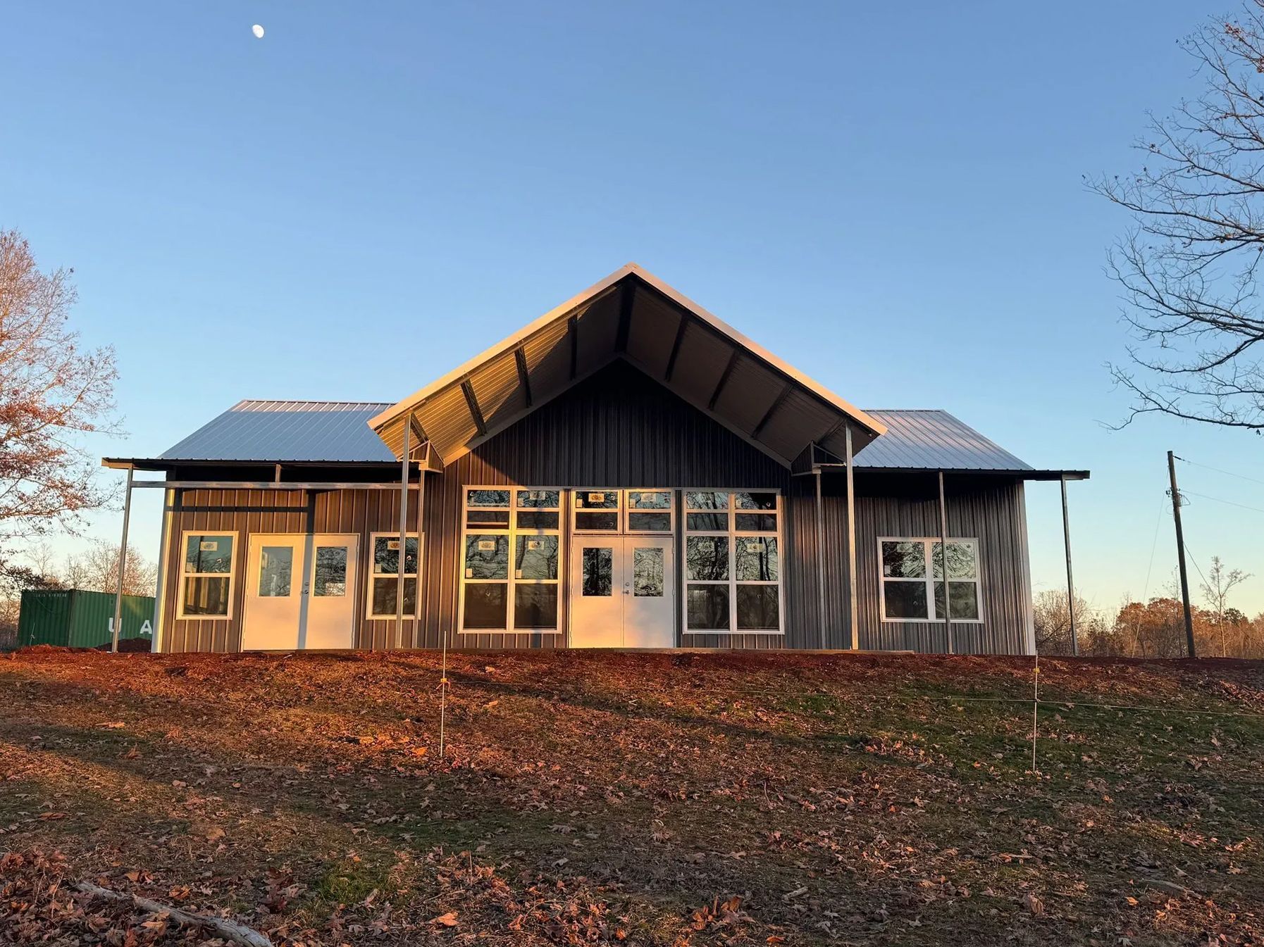 A wooden building with a high roof, large windows, and white doors against a clear blue sky.