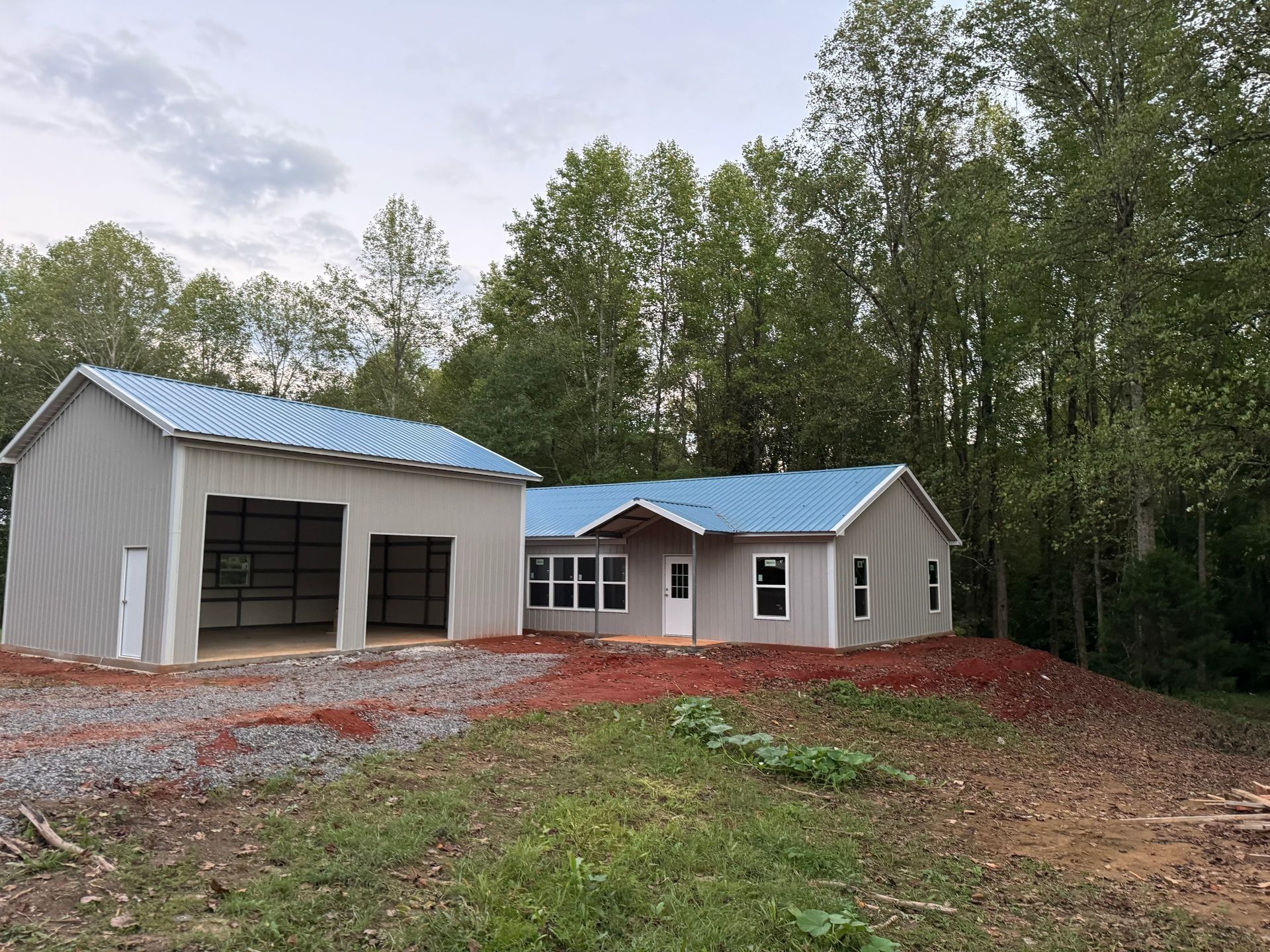 Gray house and attached garage with blue roofs in a wooded area.