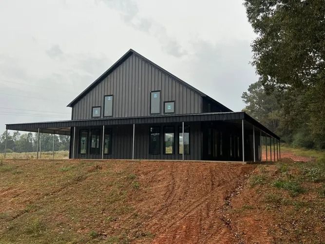 Black modern barn house with a porch on a grassy hill under a cloudy sky.