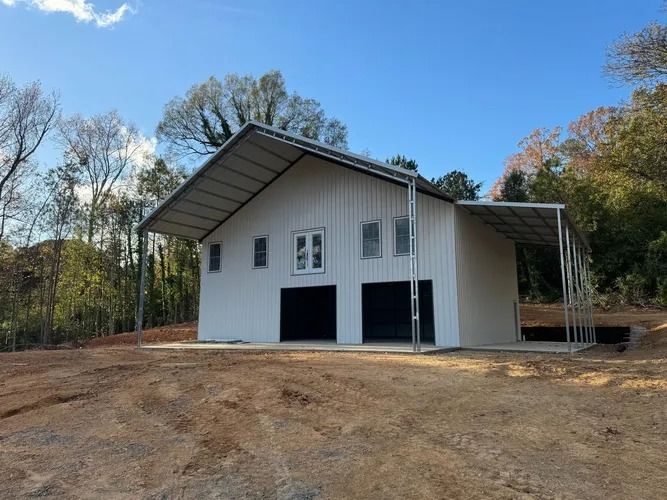 White barn with black doors under a blue sky. A metal awning extends from the right side.