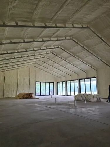 Interior of a building with spray foam insulation on walls and ceiling. Large windows, concrete floor, empty space.