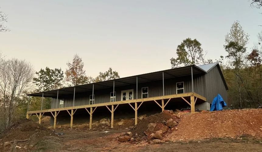 A one-story building under construction with a large porch, set on a hillside.