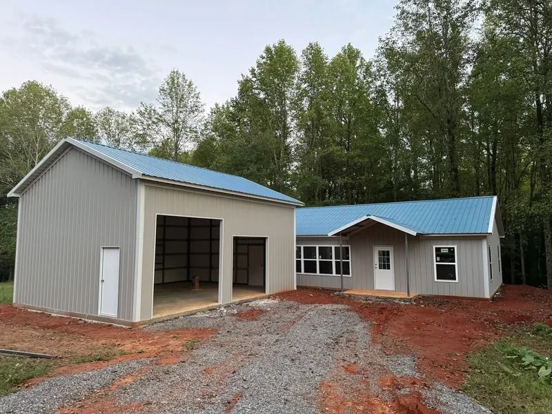 Gray home and garage with blue roofs, gravel driveway, and trees in the background.
