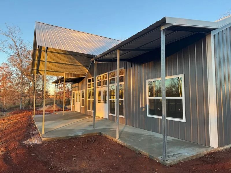 Gray metal building with covered porch and windows, set against a blue sky.
