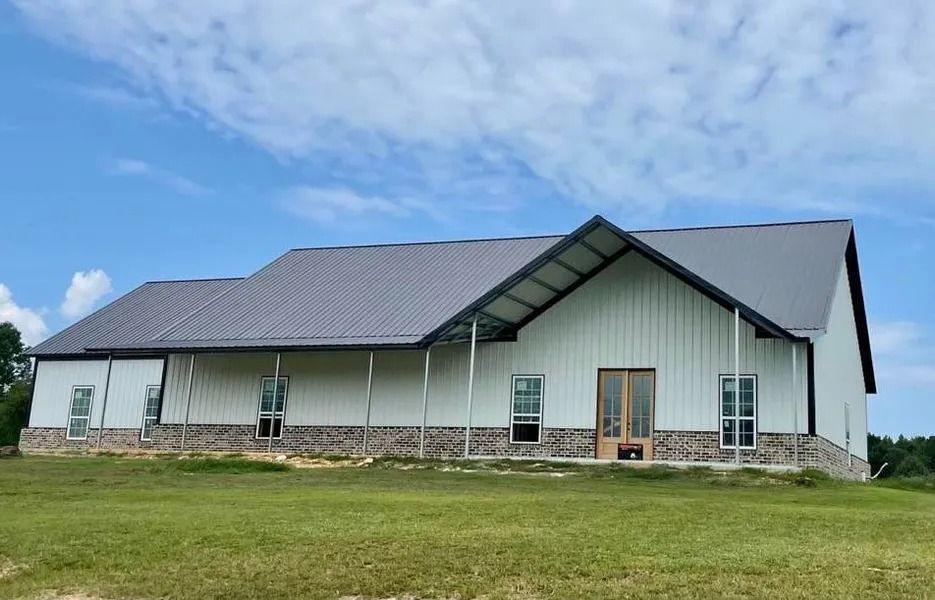 White barn-style building with a gray roof, light blue sky, and grassy field.