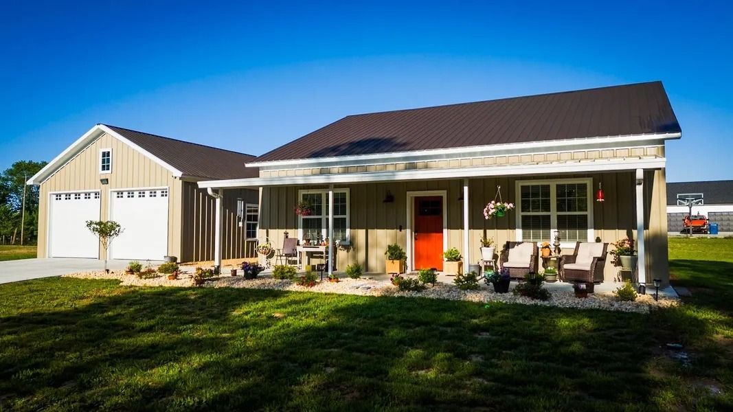 Tan house with orange door, porch with chairs, attached garage. Green yard, blue sky.