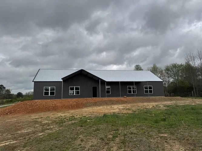 Dark gray metal-sided house with a metal roof, on a slight rise under a cloudy sky.