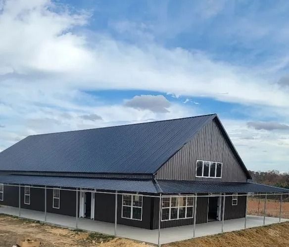 Dark gray barn-style building with a blue metal roof under a cloudy sky.