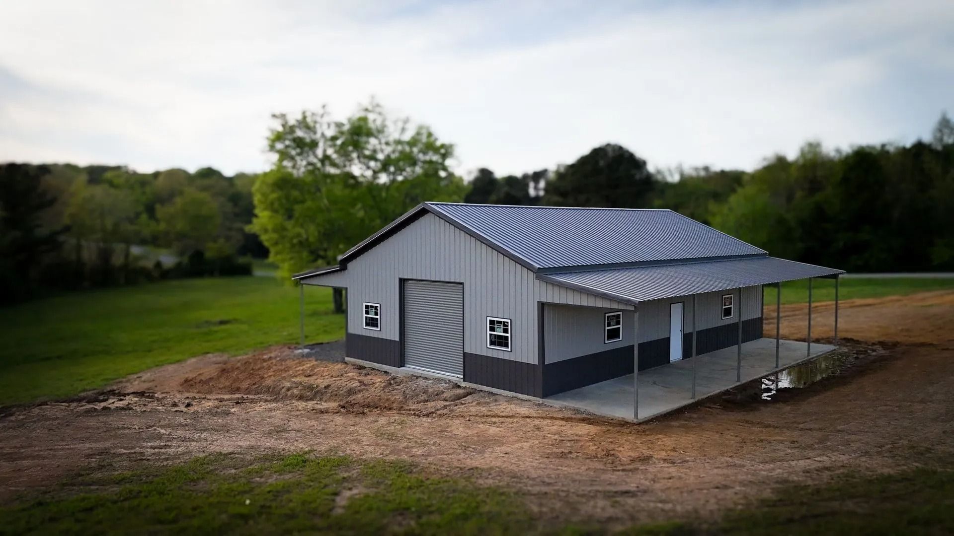 Gray and black metal barn with porch on a grassy hill.