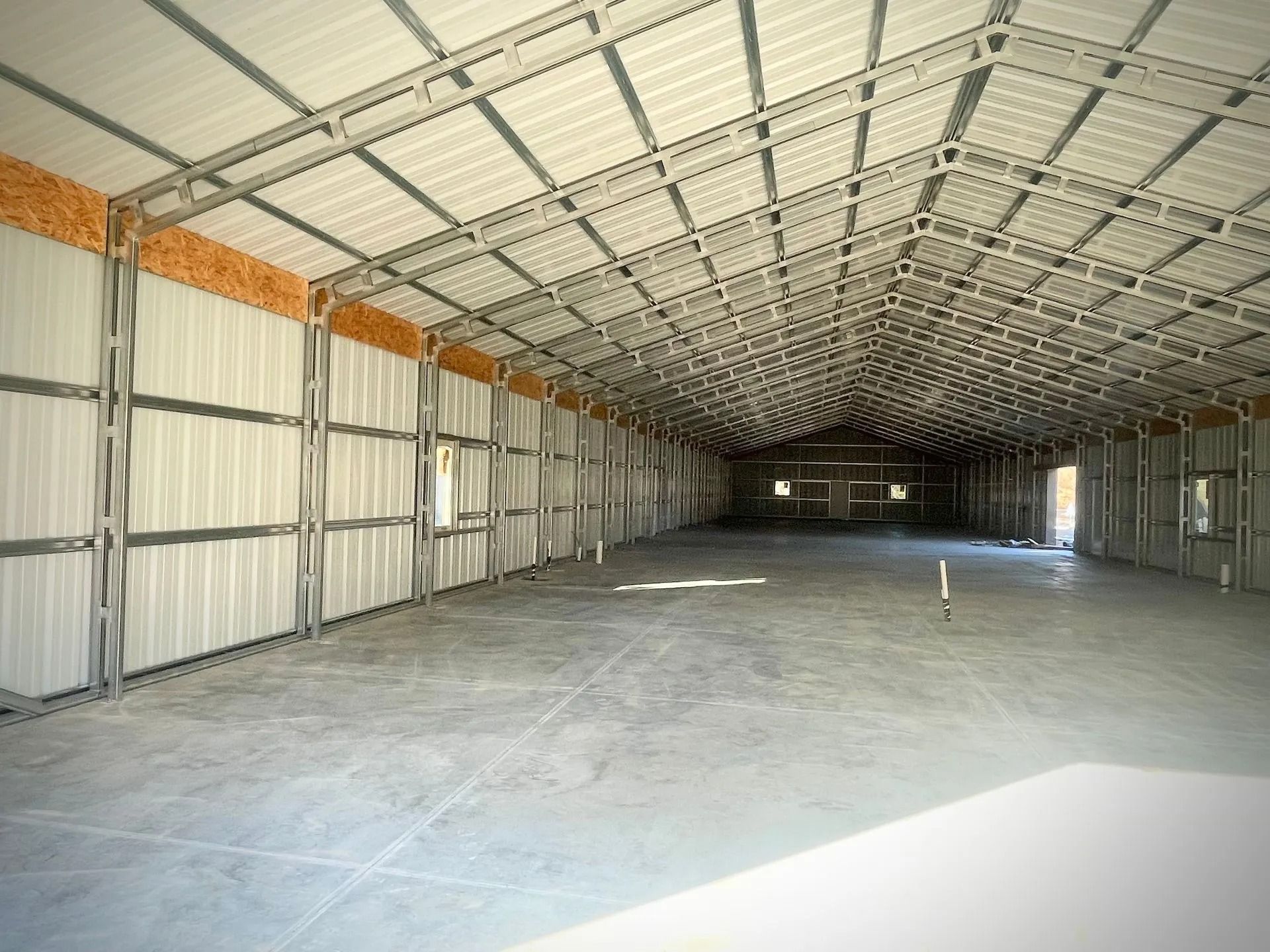 Interior view of a large, empty metal building with a concrete floor and steel framework, white roof and walls.