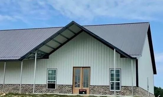 White barn with a gray roof and brick base, blue sky.