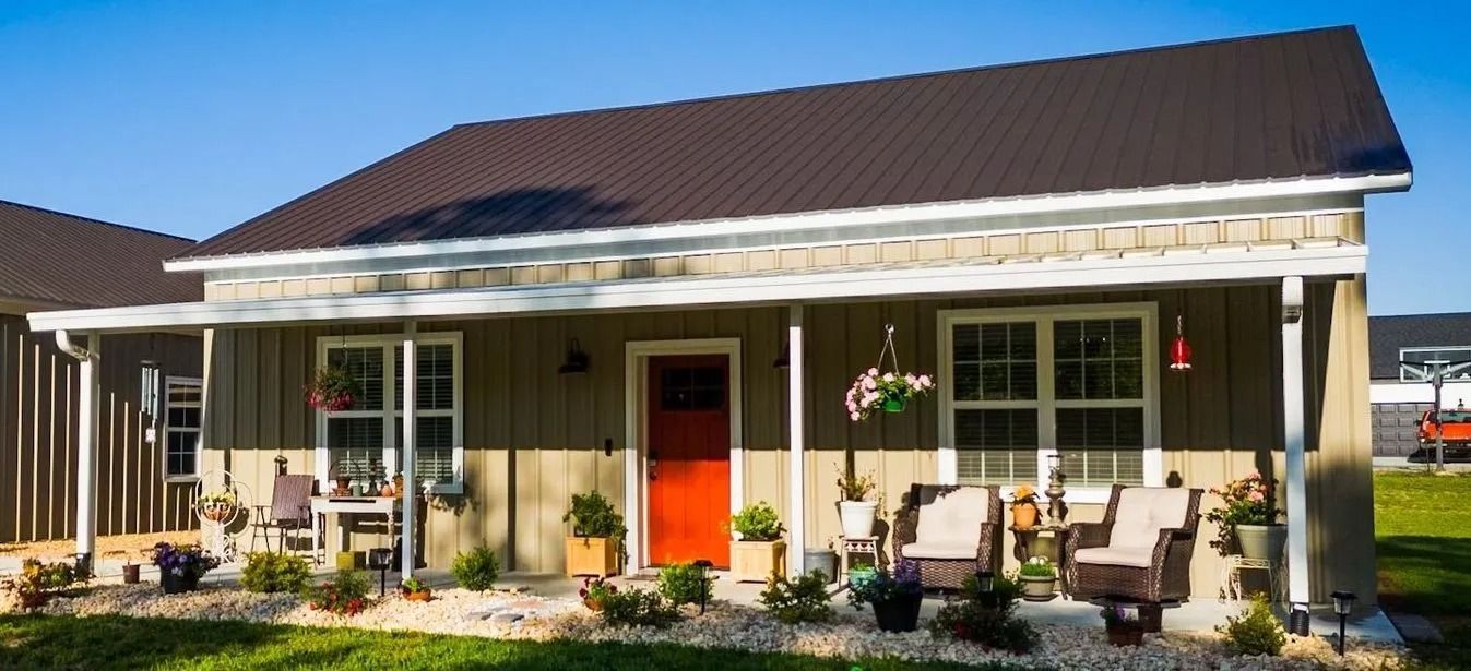 A charming small house with a red door, porch, and brown roof. Green lawn and blue sky.
