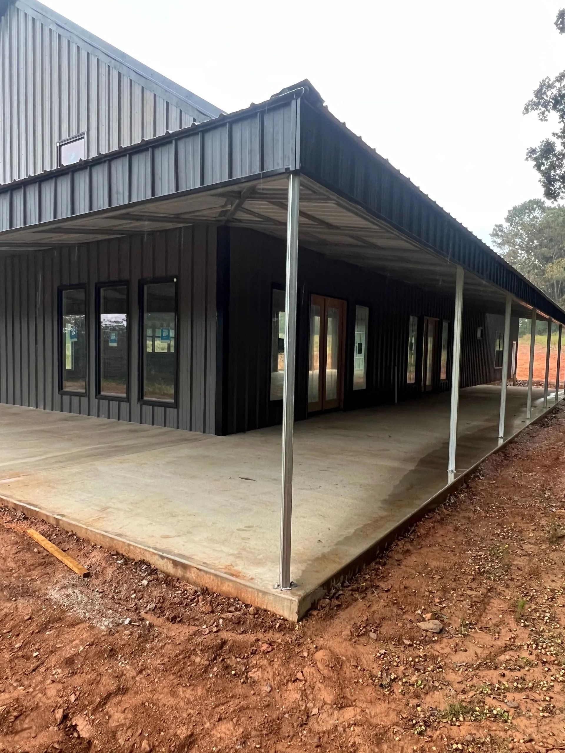 Modern building with dark gray siding, concrete porch, and metal roof.
