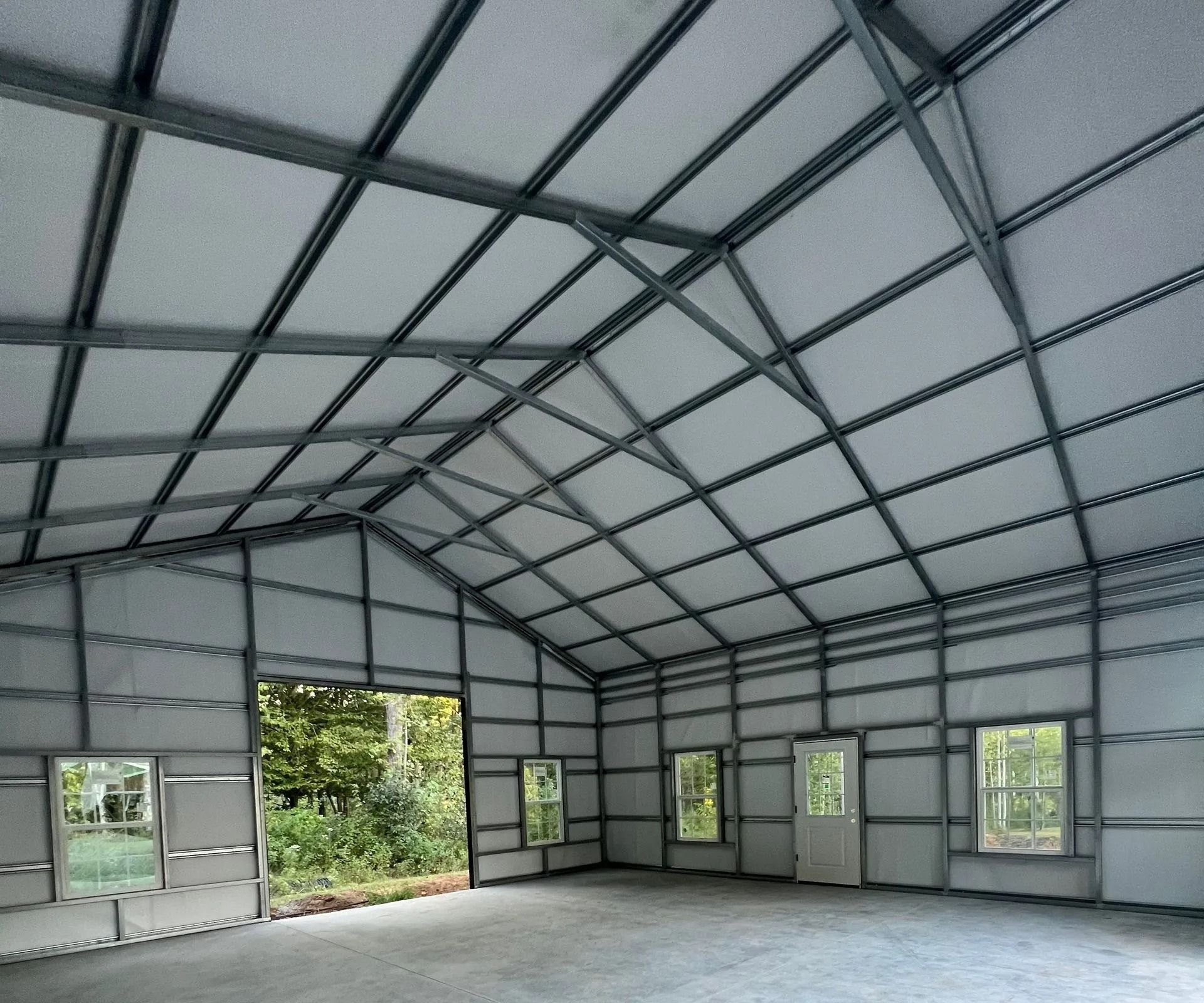 Interior view of a metal frame building with gray walls, a concrete floor, and several windows and a door.