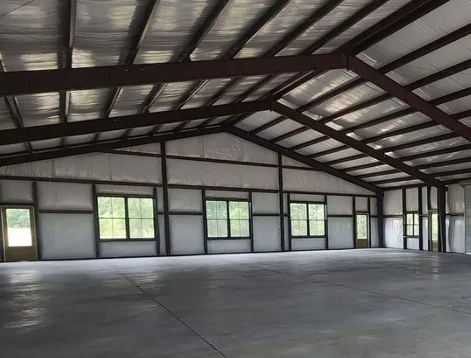 Interior of a large, empty steel-framed warehouse with windows along the walls and a concrete floor.