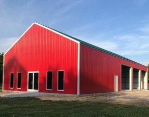Red metal barn with white trim, green roof, and open bay doors under a blue sky.