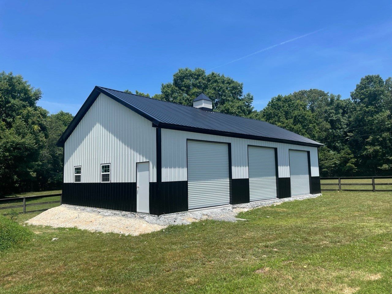 A large, black and white garage with two garage doors, a black roof, and a gravel base on a grassy lawn.
